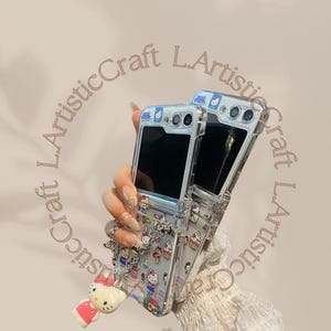 May include: Two clear phone cases with a Hello Kitty design. The cases are attached to each other with a chain. The cases are decorated with Hello Kitty characters and other cute designs.