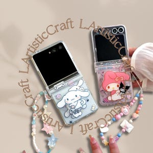 May include: Two clear phone cases, each with a cartoon character design. One case shows a white bunny, the other a pink character with a black cat. Both cases are open, displaying the phone screens. A beaded strap with charms is attached.