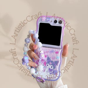 Könnte beinhalten: Eine lila und weiße Handyhülle mit einem Cartoon-Charakter-Design. Die Hülle hat eine transparente Rückseite und eine nach oben klappbare Vorderseite. Ein Perlenarmband ist an der Hülle befestigt.
