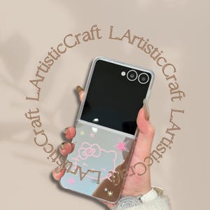 Pu&ograve; includere: Custodia trasparente per telefono con superficie a specchio con un design di Hello Kitty con stelle rosa e testo. La custodia &egrave; aperta, rivelando lo schermo e la fotocamera del telefono.