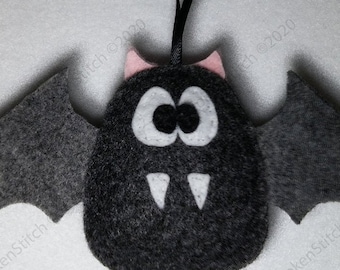 以下が含まれることがあります： ピンクの耳、白い目、白い牙が付いた黒いフェルトの蝙蝠のオーナメント。蝙蝠には、吊り下げ用の黒いリボンループが付いています。