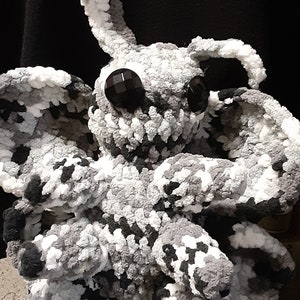 May include: A crocheted plush toy in the shape of a creature with large ears, black eyes, and a gray and white color scheme.