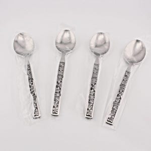 May include: Four silver-toned metal spoons arranged in a row. Each spoon features a polished oval bowl and a rectangular handle decorated with a repeating embossed floral pattern. Each individual spoon is encased in a clear plastic sleeve.