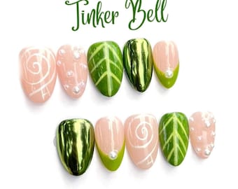 May include: A set of ten press-on nails with the text Tinker Bell at the top. The designs include light pink nails with white swirls or small white pearls, green nails with leaf vein patterns, and solid metallic green nails with a glossy finish.