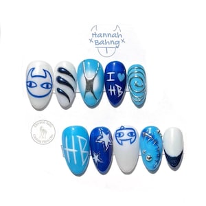 May include: A set of ten press-on nails featuring various blue and white designs, including a cartoon face, the text "I HB" with a heart, the letters "HB", silver swirls, stars, and metallic studs on a white display card with the text Hannah Bahng.