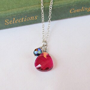 May include: A silver chain necklace with a teardrop-shaped pink crystal pendant and a smaller blue crystal accent.