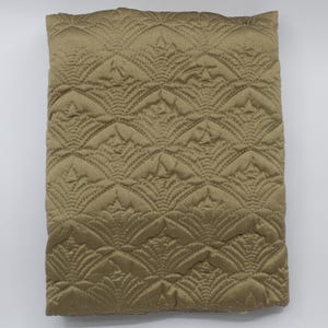 May include: A folded, golden-brown quilted fabric with a repeating fan-shaped pattern. The stitching creates a textured surface, and the fabric has a slight sheen. The overall design is symmetrical and decorative, suitable for bedding or upholstery.