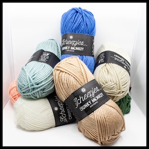 May include: A collection of colorful yarn skeins in various shades, including blue, green, beige, and cream. Each skein is labeled with the text "Scheepjes Chunky Monkey Anti Pilling". The yarn is arranged in a visually appealing display, suitable for knitting or crochet projects.