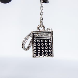 May include: A silver-colored charm in the shape of a vintage calculator, with a black keypad and a small handle. The charm is suspended from a delicate chain, perfect for jewelry or accessories.