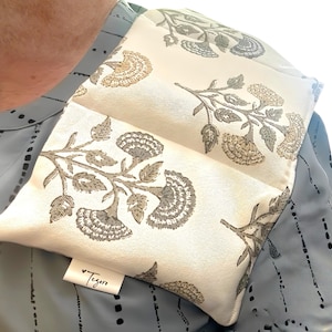 May include: A cream-colored shoulder wrap with a floral pattern in shades of gray and tan. The wrap is rectangular and appears to be made of fabric. The label reads "Tegoro".