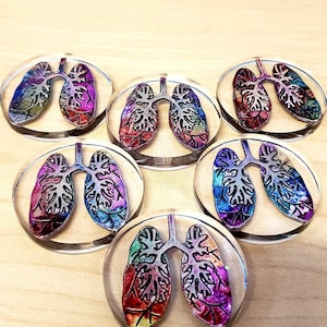 May include: Six colorful resin cabochons with a rainbow iridescent finish, each featuring a black outline of a pair of lungs.
