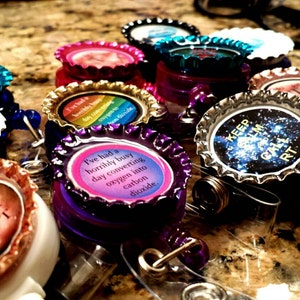 May include: A collection of colorful bottle cap badge reels with various sayings, including "Keep Calm and Carry On", "Tube Those", and "I've had a horribly busy day converting oxygen into carbon dioxide".