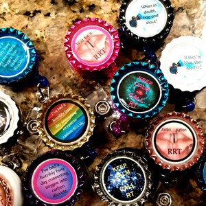 May include: A collection of colorful, round, plastic badge holders with various respiratory therapy-related sayings and images. The sayings include "Keep Calm and Call RT", "If they're blue, they need O2", "I've had a horribly busy day converting oxygen into carbon dioxide", and "Wait for it... RRT".