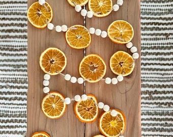 May include: A garland made of dried orange slices and white wooden beads. The garland is laid out on a wooden surface.