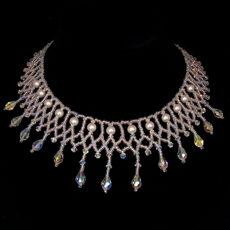 May include: A delicate beaded necklace with a diamond-shaped pattern, featuring iridescent beads and faux pearls. The necklace has dangling crystal pendants and a black background.