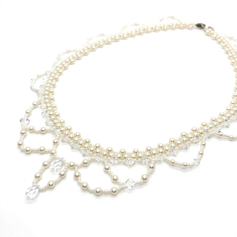 May include: A delicate necklace featuring faux pearls and clear crystal accents. The necklace has a layered design with a scalloped bottom edge. The pearls are small and round, and the crystals are faceted and teardrop-shaped.