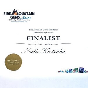 May include: A certificate from Fire Mountain Gems and Beads, featuring the text "FINALIST" and the name "Noelle Kostraba." The certificate includes the company logo and details about the 2009 Beading Contest. A gold seal is also present.