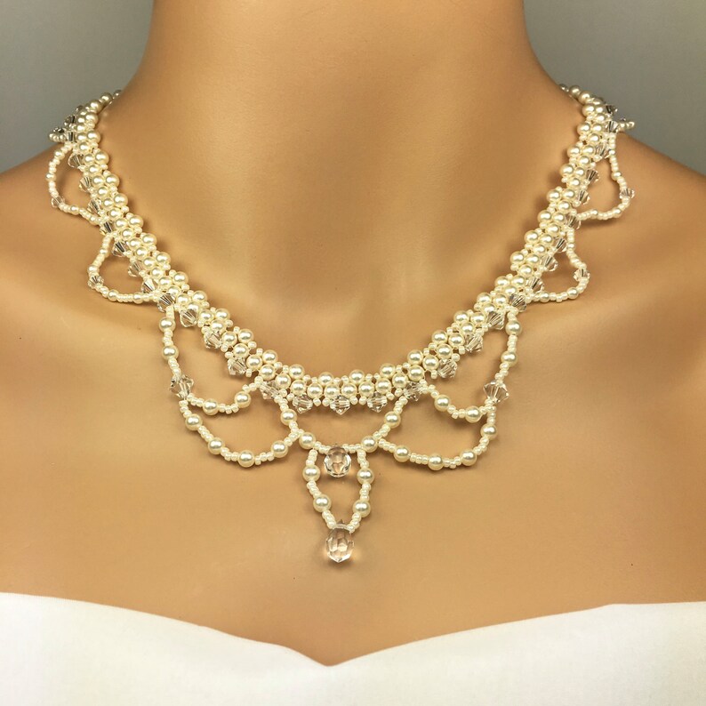 May include: An ivory-colored necklace featuring faux pearls and clear crystal accents. The necklace has a bib-style design with multiple strands of pearls and dangling crystals, creating a delicate and elegant look. The necklace is designed to be worn around the neck.