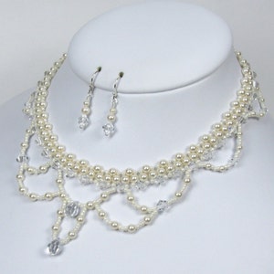 May include: An elegant necklace and earring set. The necklace features multiple strands of cream-colored faux pearls and clear crystal accents. The earrings are a matching design with a single crystal drop. The jewelry is displayed on a white bust.