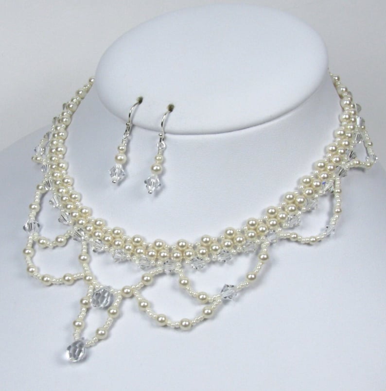 May include: An elegant necklace and earring set. The necklace features multiple strands of cream-colored faux pearls and clear crystal accents. The earrings are a matching design with a single crystal drop. The jewelry is displayed on a white bust.