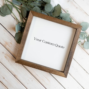 May include: A square wooden frame with a dark brown finish surrounding a white center panel. The text "Your Custom Quote" is printed in black, serif lettering in the middle of the white space. The frame is positioned at an angle.