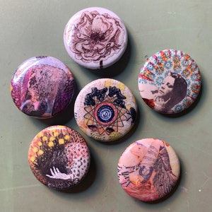 May include: Six round, colorful, printed buttons with various designs. The buttons feature a flower, a person's face, a geometric design, a floral design, a person's face, and a geometric design.