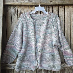 May include: A button-down cardigan sweater in a soft, multi-colored knit. The sweater features a blend of pastel colors, including gray, pink, and blue. It has long sleeves and a round neckline. The sweater is hanging on a white hanger.