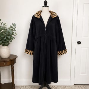 May include: A black zip-up robe featuring a long silhouette, long sleeves, and a fold-over collar. The collar and the sleeve cuffs are accented with a tan and black tiger stripe pattern. The garment is displayed on a mannequin torso.