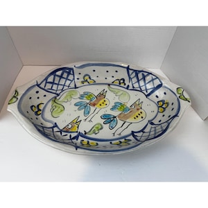 May include: Oval ceramic serving platter with a hand-painted bird design. The platter features a white base with blue and green accents, and a rim with a blue lattice pattern. The birds are yellow, blue, and brown.
