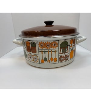 May include: A vintage brown and white enamel cooking pot with a matching lid. The pot features a decorative pattern of flowers, kitchen utensils, and other kitchen-themed illustrations. It has two white handles and a black knob on the lid.
