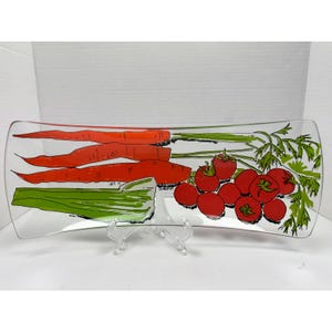 May include: A clear, rectangular serving platter with rounded ends. The platter features a colorful illustration of carrots, celery, and tomatoes. The carrots are orange with green tops, the celery is green, and the tomatoes are red. The design is in a retro style.