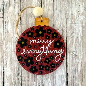 May include: A red and black Christmas ornament with a white floral pattern and the text "merry everything".