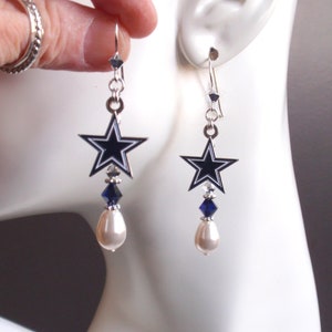 May include: Silver dangle earrings featuring a blue and white star charm, a blue crystal, and a white pearl.