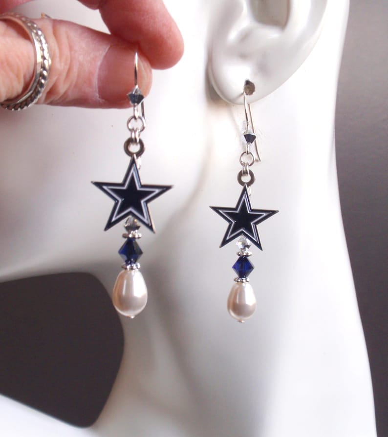 May include: Silver dangle earrings featuring a blue and white star charm, a blue crystal, and a white pearl.