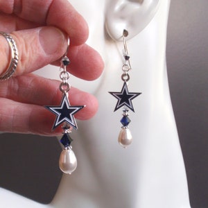 May include: Silver dangle earrings featuring a blue and white star charm with a pearl and blue crystal drop.