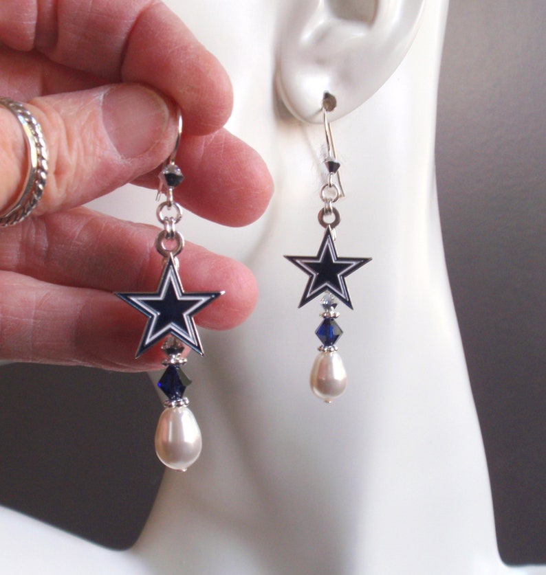 May include: Silver dangle earrings featuring a blue and white star charm with a pearl and blue crystal drop.