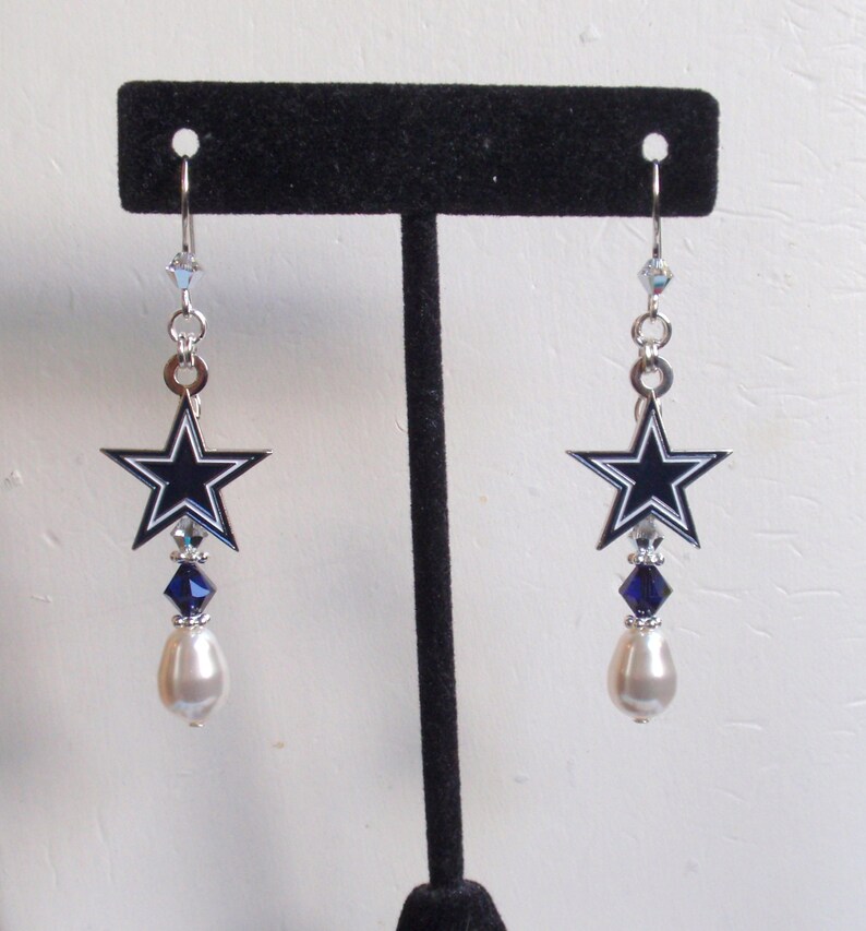 May include: A pair of silver dangle earrings featuring a blue and white star charm with a pearl and crystal accents.