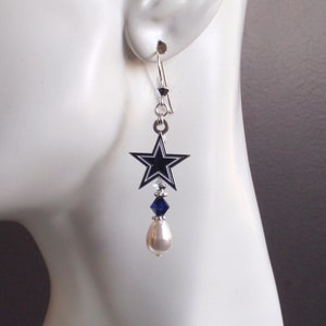 May include: Silver dangle earrings with a blue star charm, a blue crystal, and a white pearl.