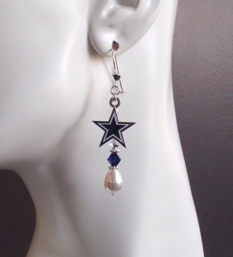 May include: Silver dangle earrings with a blue star charm, a blue crystal, and a white pearl.