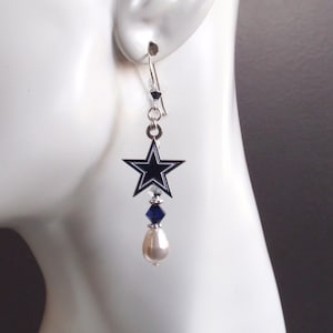 May include: Silver dangle earrings featuring a black and white star charm with a blue crystal and a white pearl.