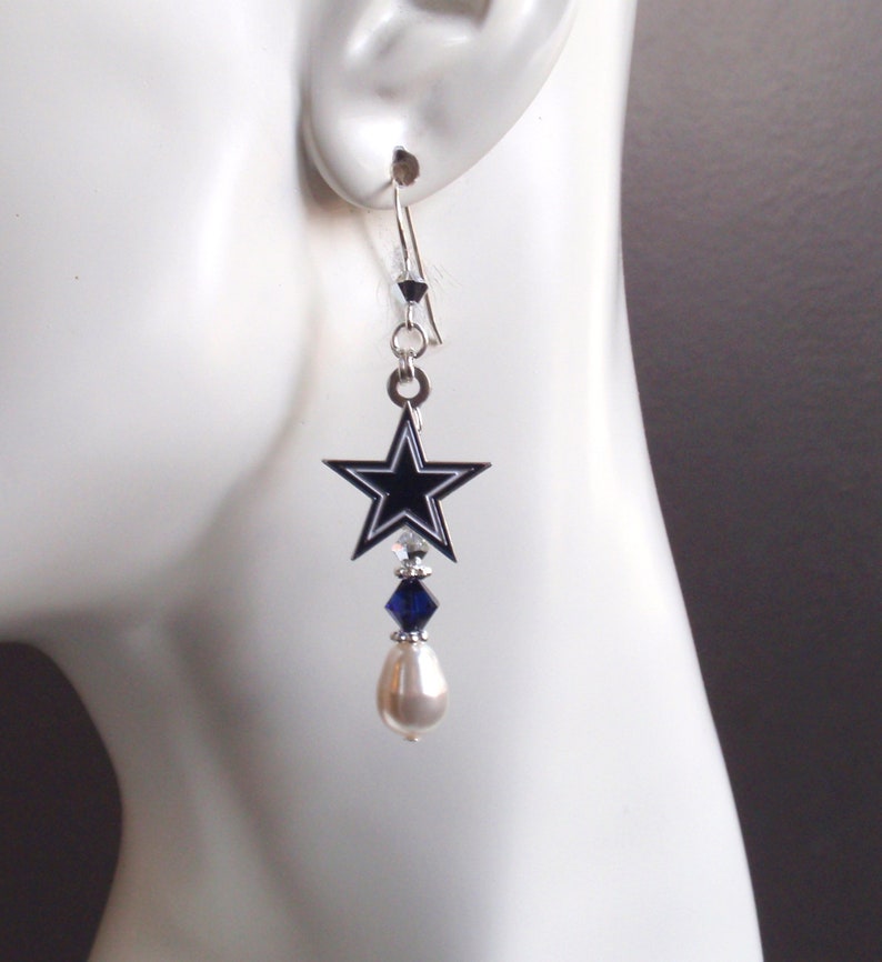May include: Silver dangle earrings featuring a black and white star charm with a blue crystal and a white pearl.