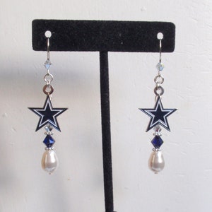 May include: Silver dangle earrings with a blue and white star charm, a blue crystal, and a white pearl.