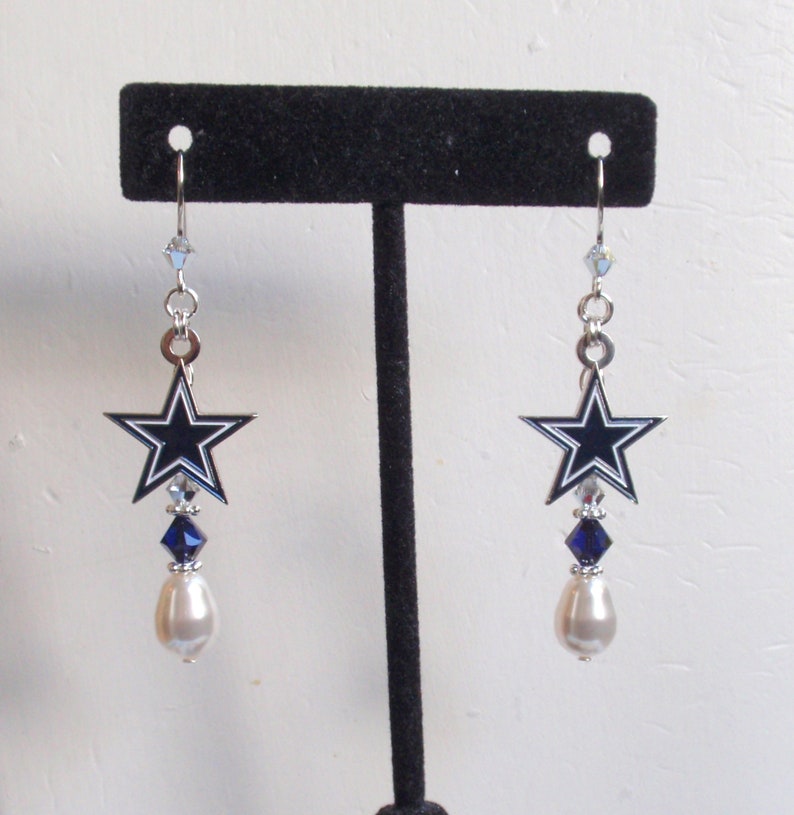 May include: Silver dangle earrings with a blue and white star charm, a blue crystal, and a white pearl.