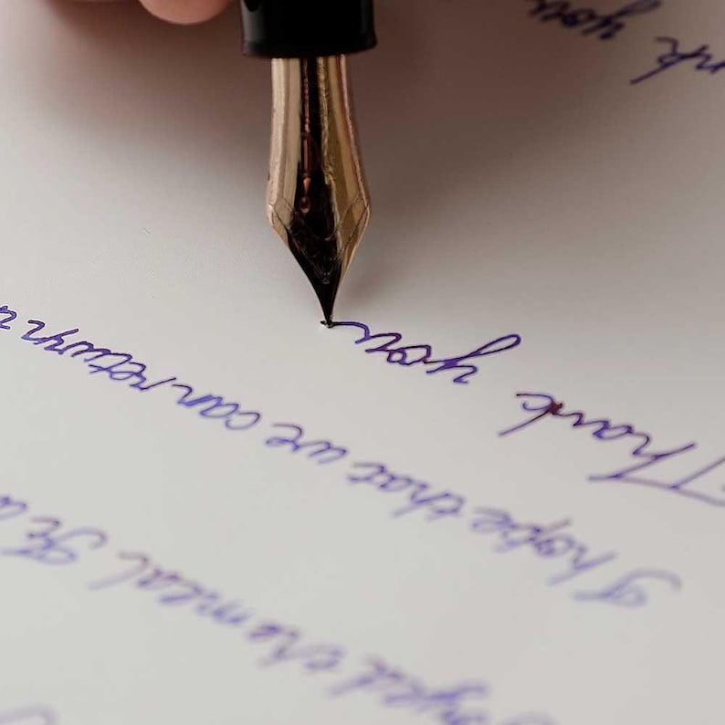 May include: A close-up of a fountain pen with a gold nib writing on a white piece of paper. The pen is being held by a hand, and the paper has blue ink on it. The text on the paper reads "Thank you" and "I hope that we can return to normal soon."