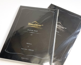 May include: Two black paper pads with gold lettering. The front pad says "Tomoe River Paper Pad A5 100 Sheets X Paper Color: CREAM Made in Japan".