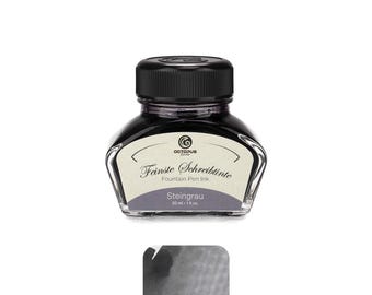 May include: A clear glass bottle filled with dark gray fountain pen ink, featuring a black screw-top lid and a cream-colored label. The label displays the text Octopus Fluids, Feinste Schreibtinte, Fountain Pen Ink, Steingrau, and 30 ml - 1 fl.oz.