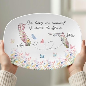 May include: An oval ceramic plate featuring floral designs and state outlines of California and Florida. The plate includes the text "Our hearts are connected, No matter the distance." Butterflies and the names "Mom" and "Daisy" are also featured.