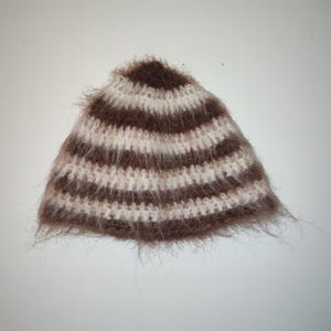 May include: A brown and white striped knit hat with a fuzzy texture.