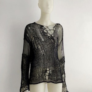 May include: Black, open-weave sweater with a distressed design. The long-sleeved top features a loose, net-like construction with intentional holes throughout. The neckline has a unique, crisscross detail. The sweater is displayed on a mannequin against a white background.