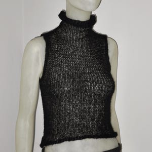 Op de afbeelding: Zwarte mouwloze coltrui. De top is gemaakt van los gebreid materiaal, met een hoge, gerimpelde halslijn en een licht verkorte zoom. Het kledingstuk wordt op een mannequin getoond.